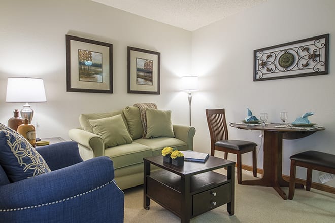 A cozy living room with a sofa, armchair, and coffee table, complemented by framed artwork and a floor lamp.