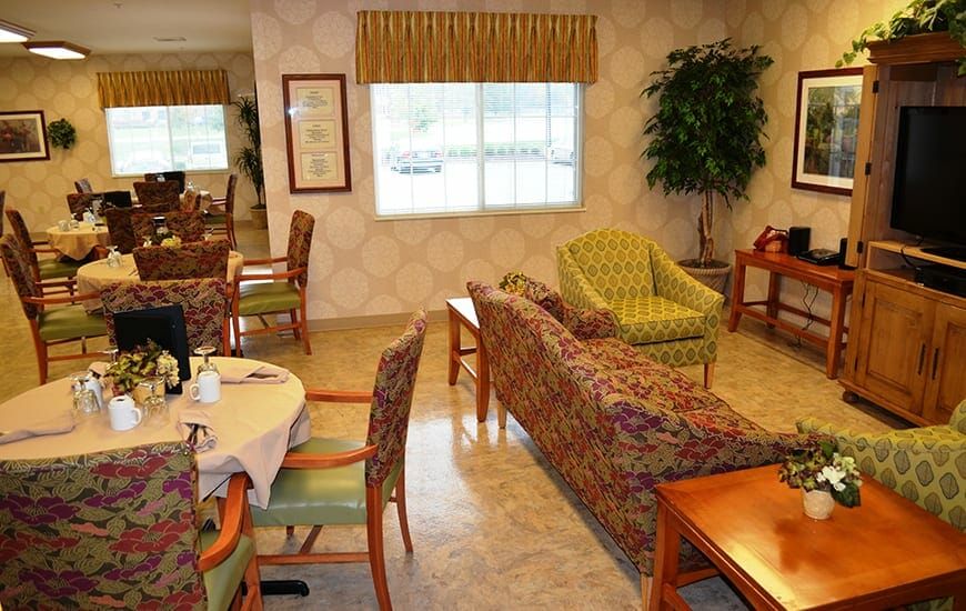 A cozy seating area with patterned chairs and sofas, a table set for dining, and a large window.