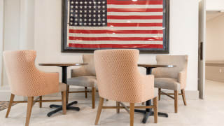 A seating area with chairs and tables is set against a backdrop of a framed American flag.