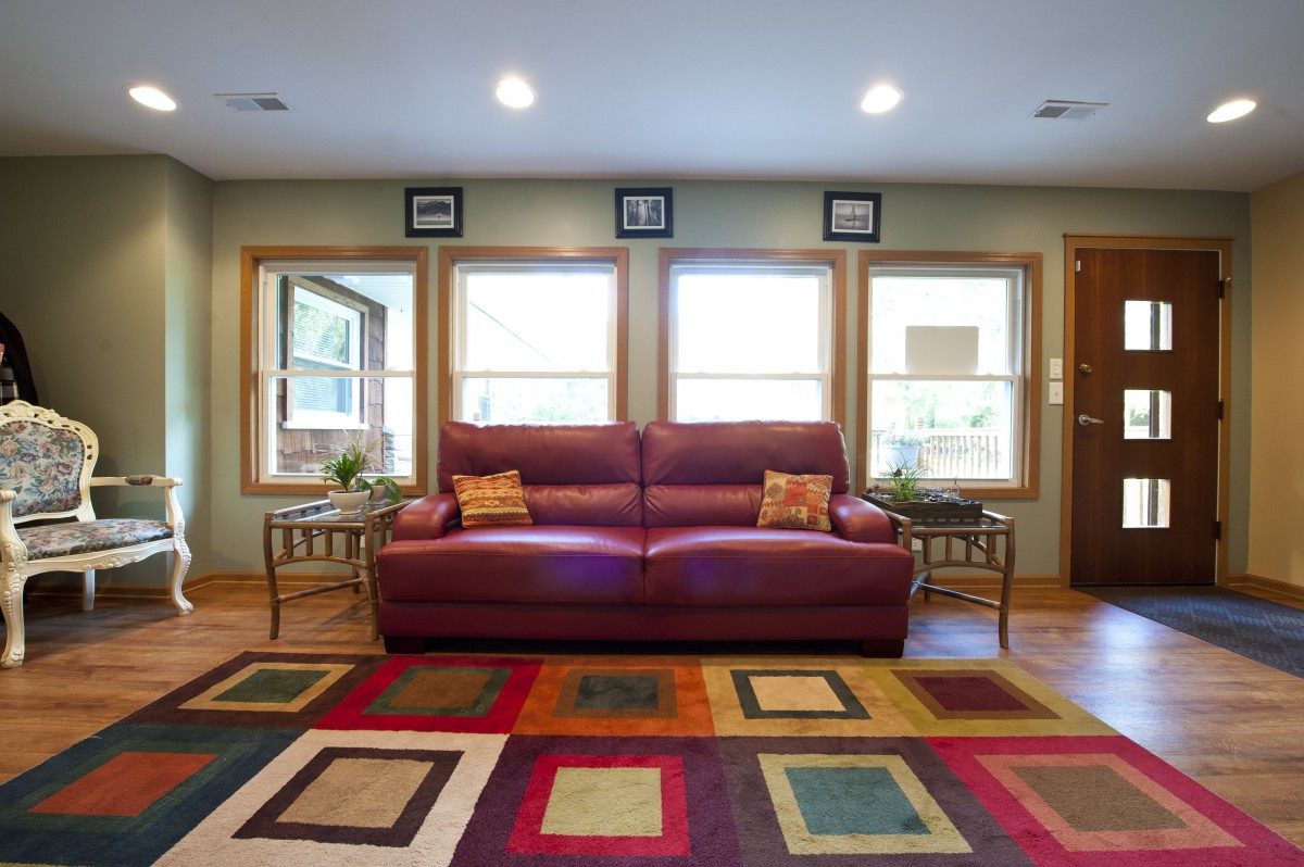 A cozy living room featuring a red sofa, colorful geometric rug, and large windows.