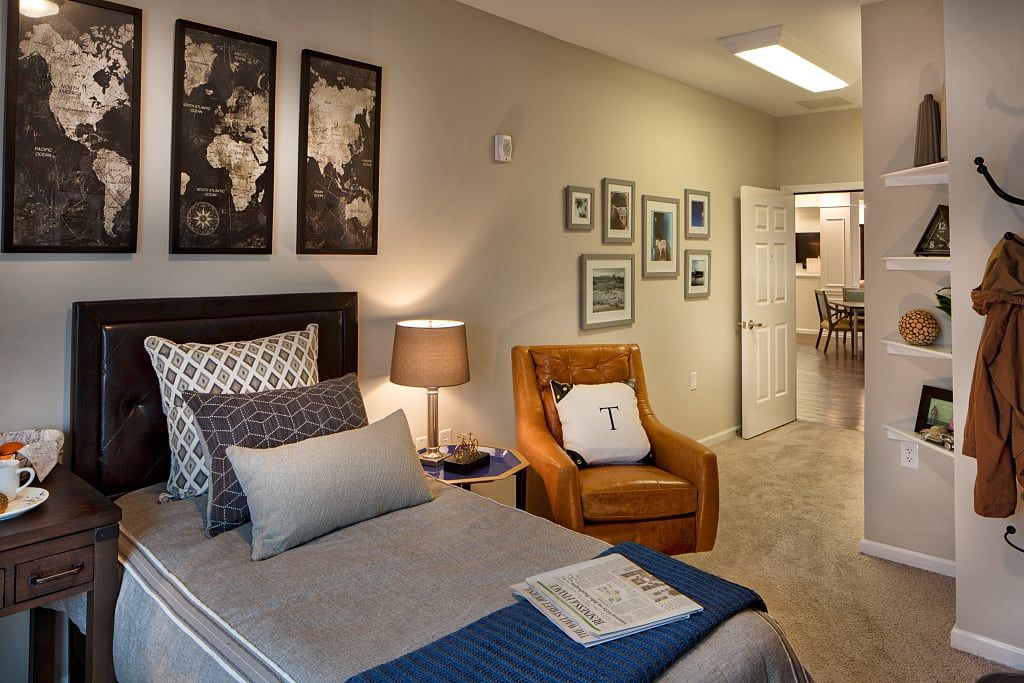 A modern and cozy bedroom featuring a neatly made bed, an orange armchair, and decorative artwork on the walls.