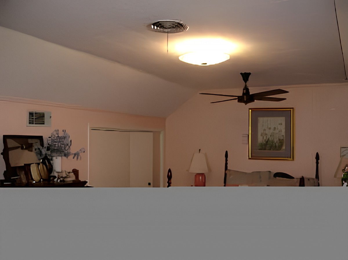 A cozy bedroom with a ceiling fan, bedside lamp, and framed painting on the wall.
