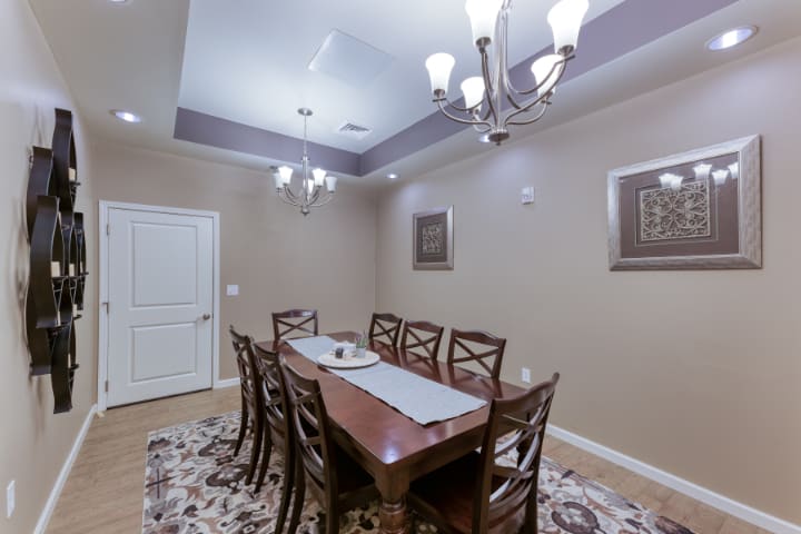 A well-appointed dining room featuring a long wooden table surrounded by chairs, with elegant chandeliers and framed artwork adorning the walls.