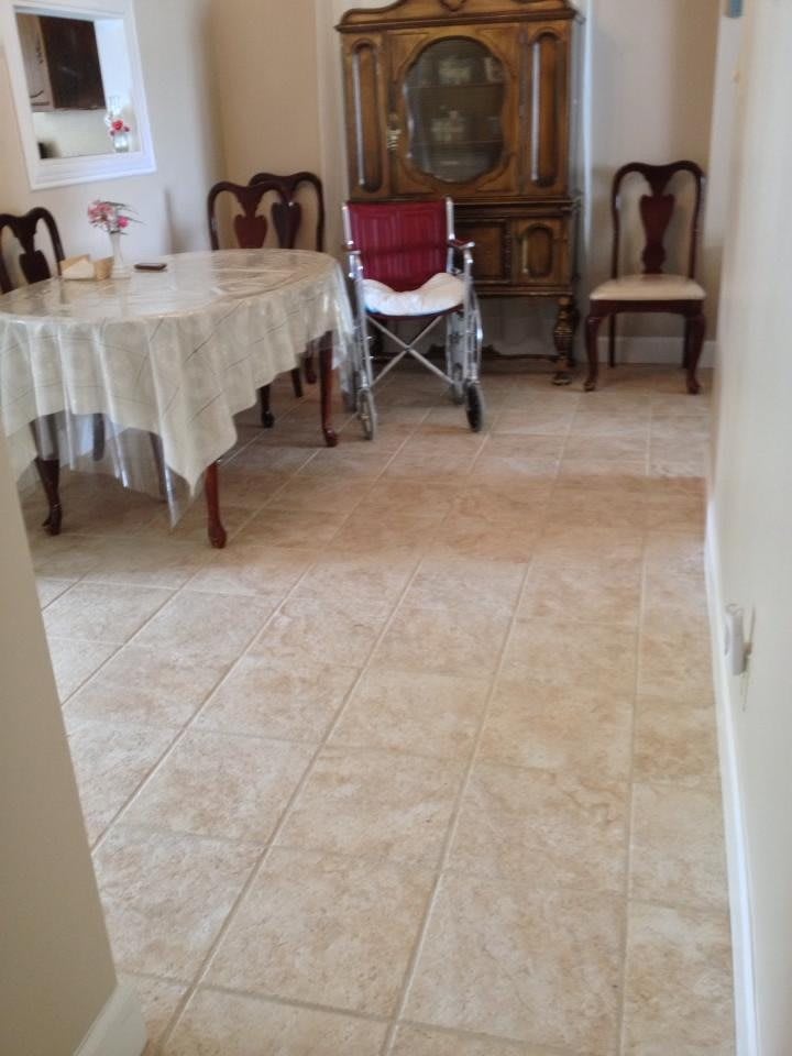 A dining room with a table, chairs, a stroller, and a tiled floor.