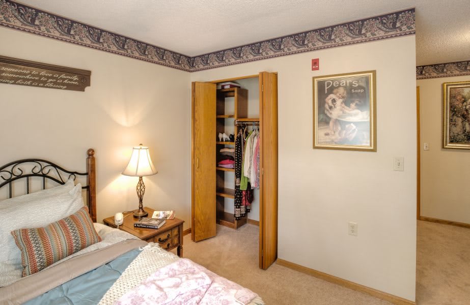 A cozy bedroom with an open closet, a bedside table with a lamp, and a painting on the wall.