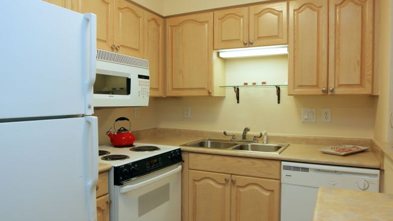 A compact kitchen with wooden cabinets, a stove, microwave, and a double sink.