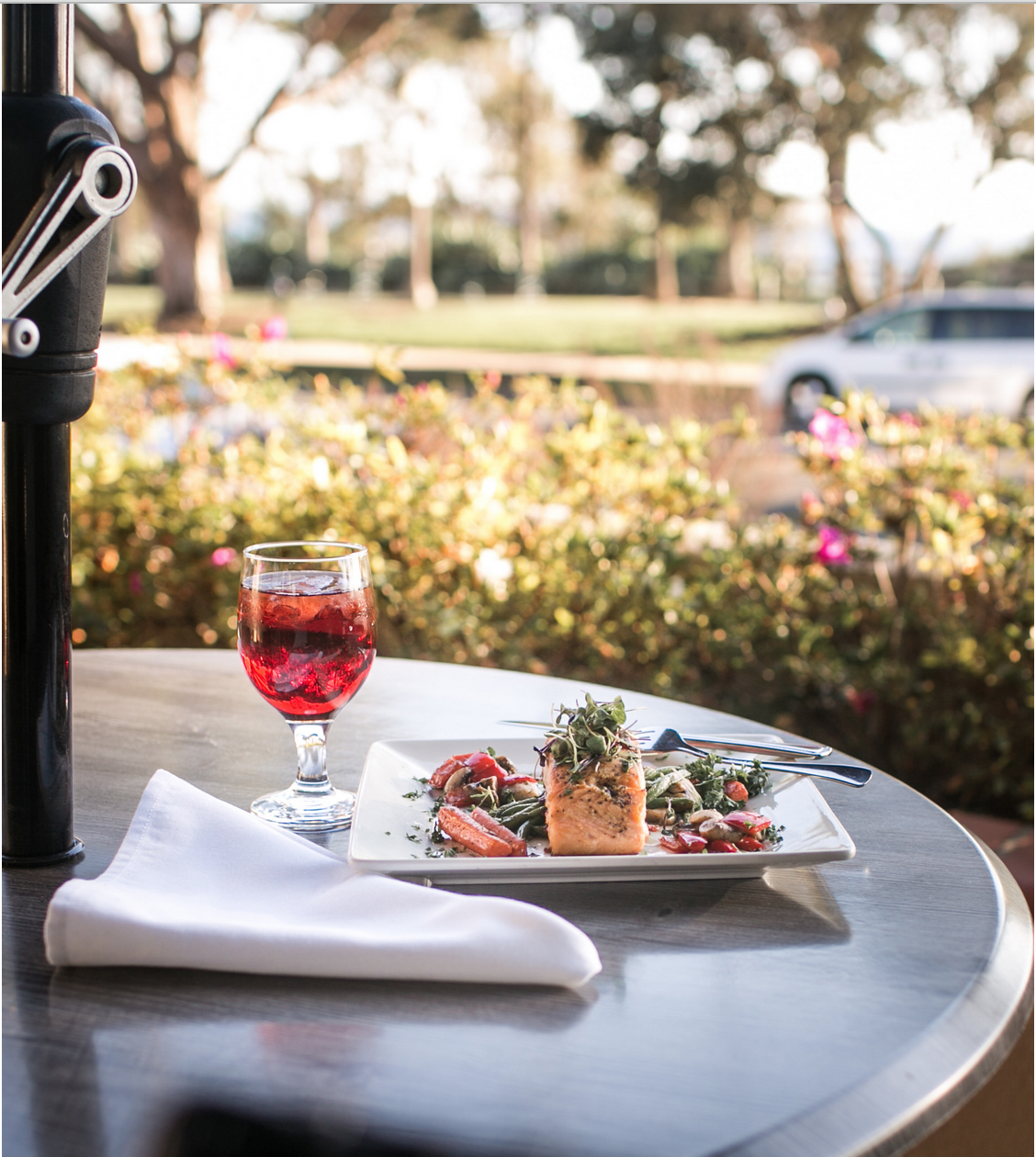 A beautifully set outdoor dining table featuring a gourmet dish and a glass of wine.