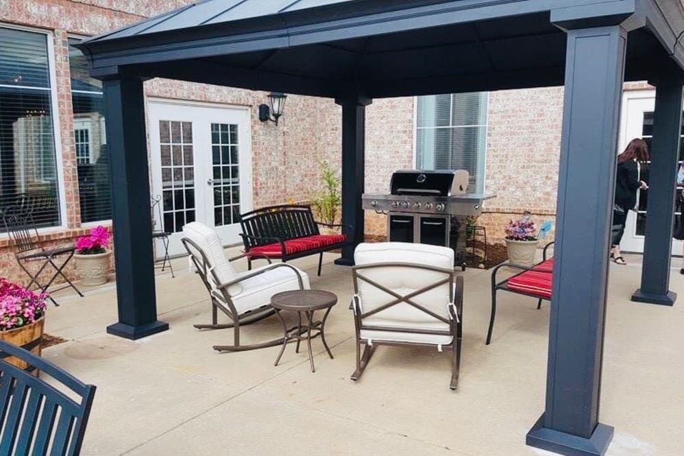 A cozy outdoor patio setup with a pergola, chairs, a table, and a grill.