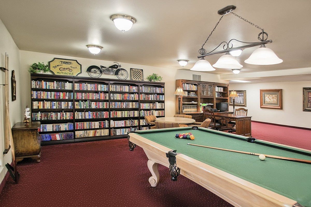 A cozy room featuring a billiards table and a large bookshelf filled with books.