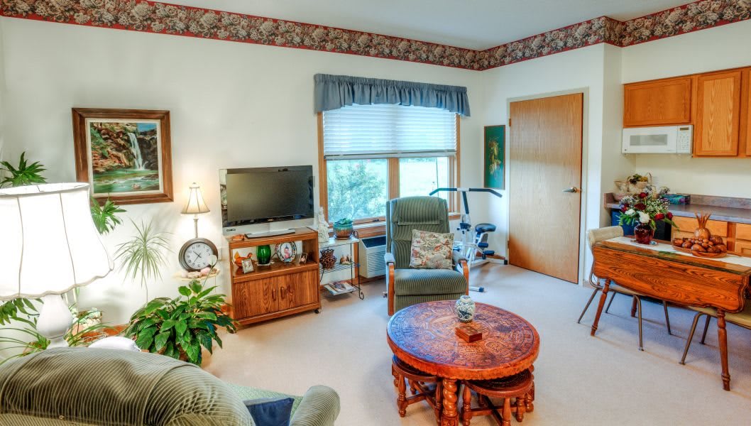 A cozy living room with a television, chairs, and a wooden table by the window.