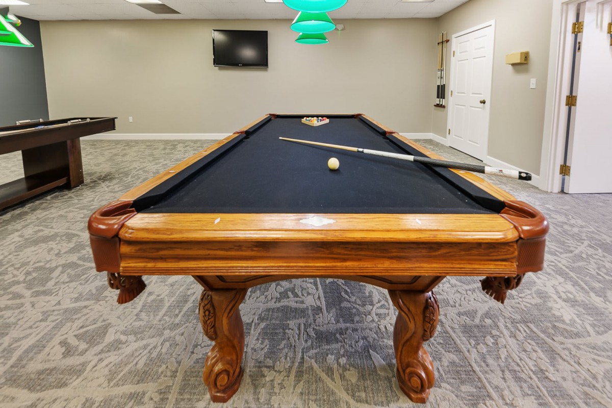 A well-maintained billiards room featuring a wooden pool table with a black felt surface.