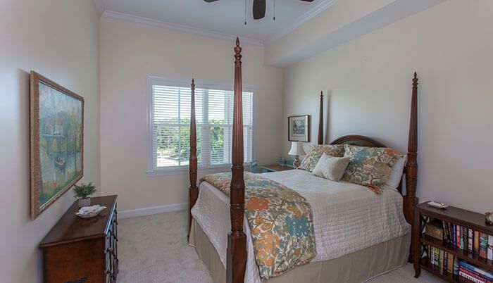 A cozy bedroom with a four-poster bed, featuring colorful bedding and pillows, complemented by a large window letting in natural light.