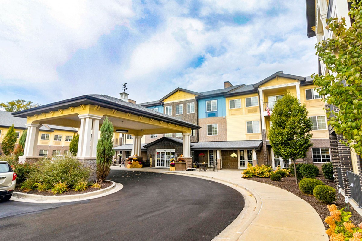 A view of a hotel entrance with a covered driveway and landscaped surroundings.