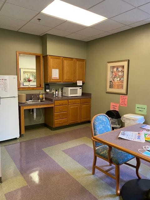 A small break room with a kitchenette, including a refrigerator and microwave, alongside a dining table and chairs.