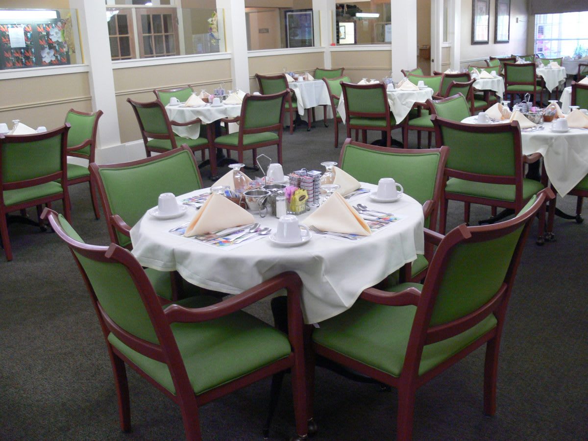 A neatly set dining table with green chairs in a restaurant.