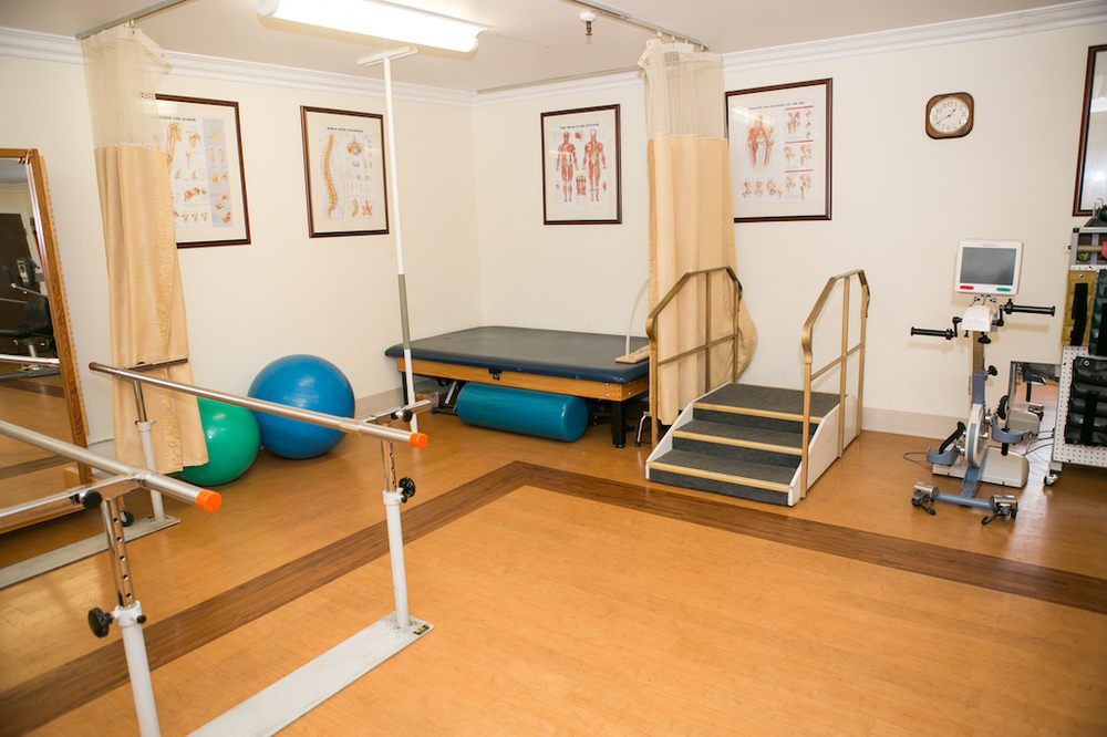 A physical therapy room equipped with exercise equipment, including parallel bars and a therapy table.