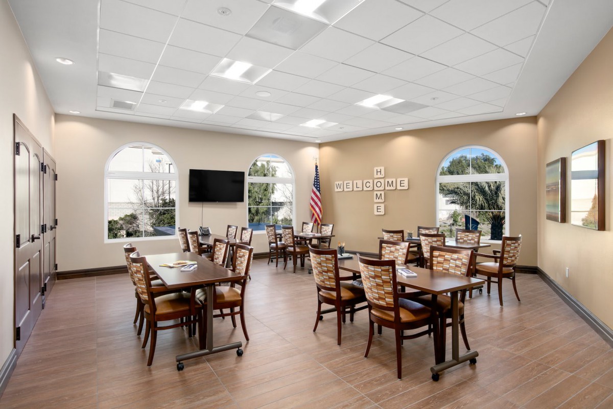 A modern dining room with neatly arranged tables and chairs, featuring a television and an American flag.
