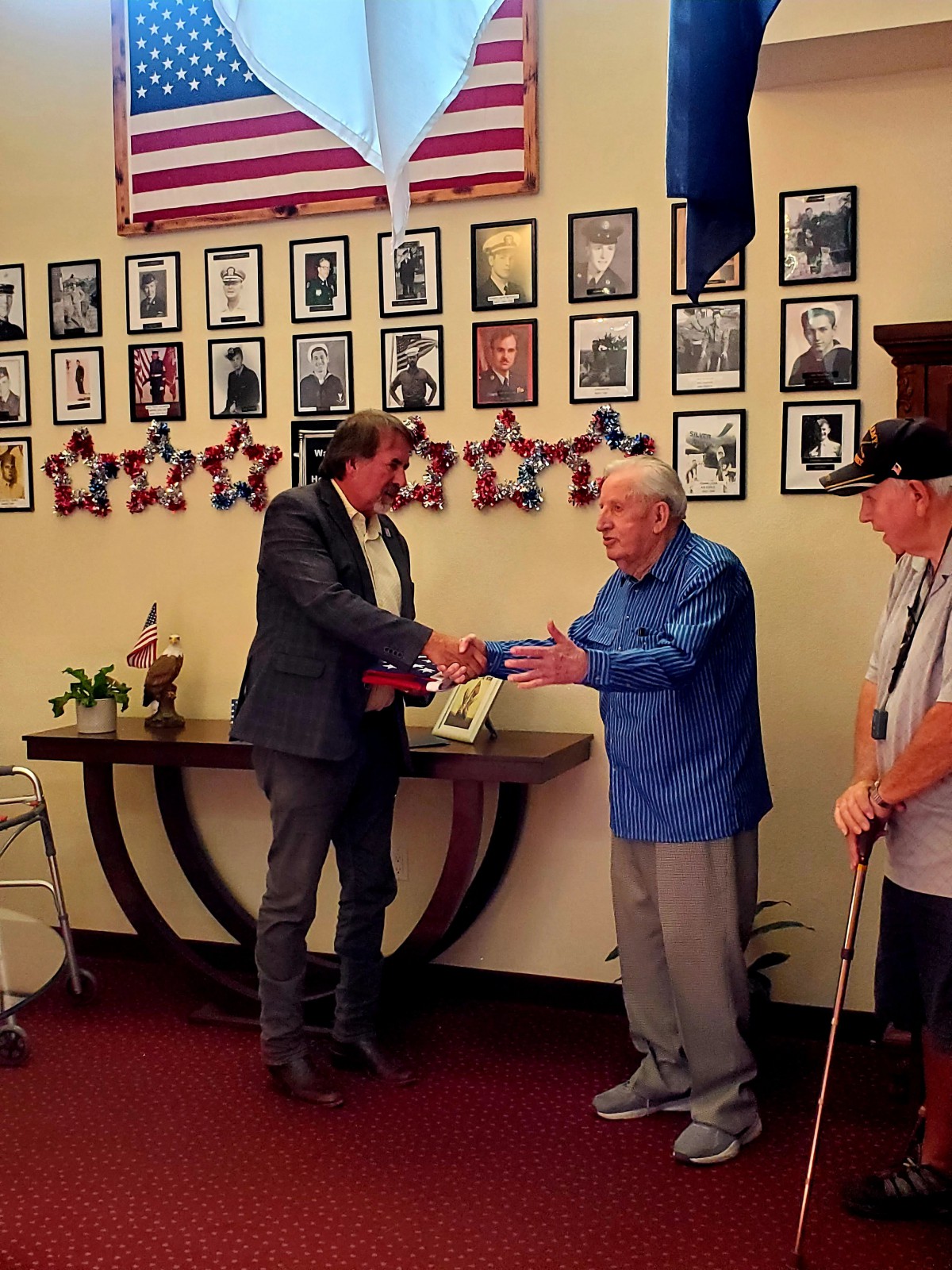 A man presents an award during a ceremony, with photographs displayed on the wall behind them.