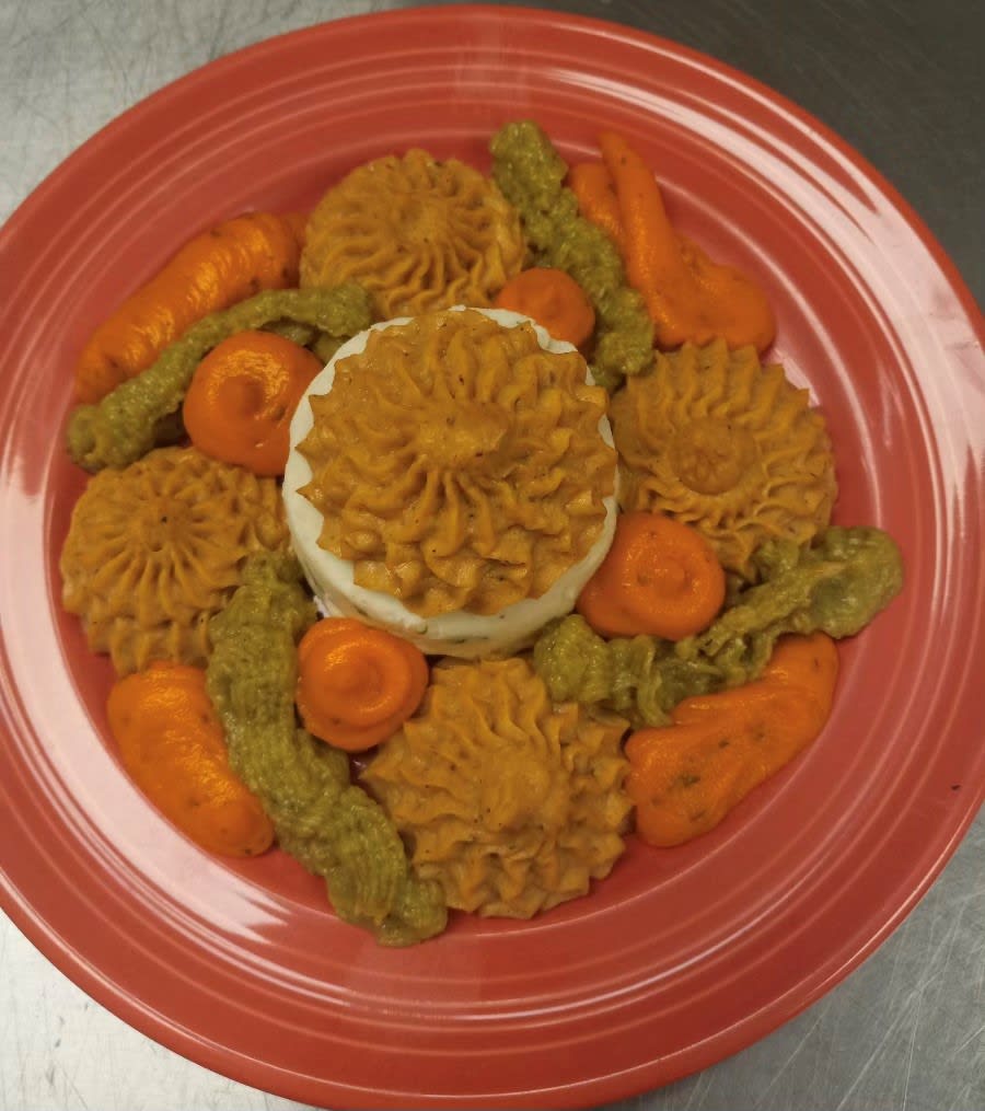 A colorful gourmet dish featuring artfully arranged vegetables and other ingredients on a red plate.