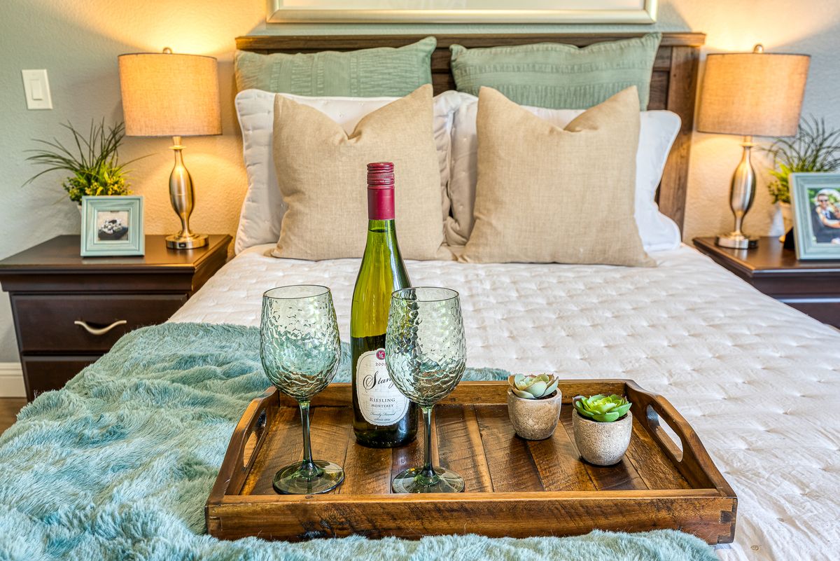 A cozy bedroom setup with a wooden tray holding a wine bottle and glasses on the bed.