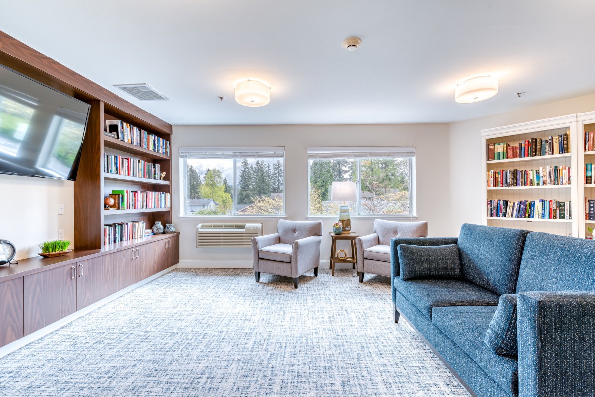 A bright living room with a large bookshelf, comfortable seating, and ample natural light.