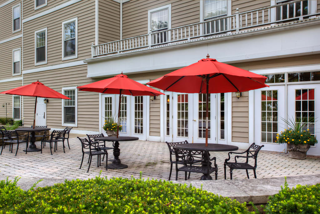 An outdoor patio area with tables, chairs, and red umbrellas in front of a building.