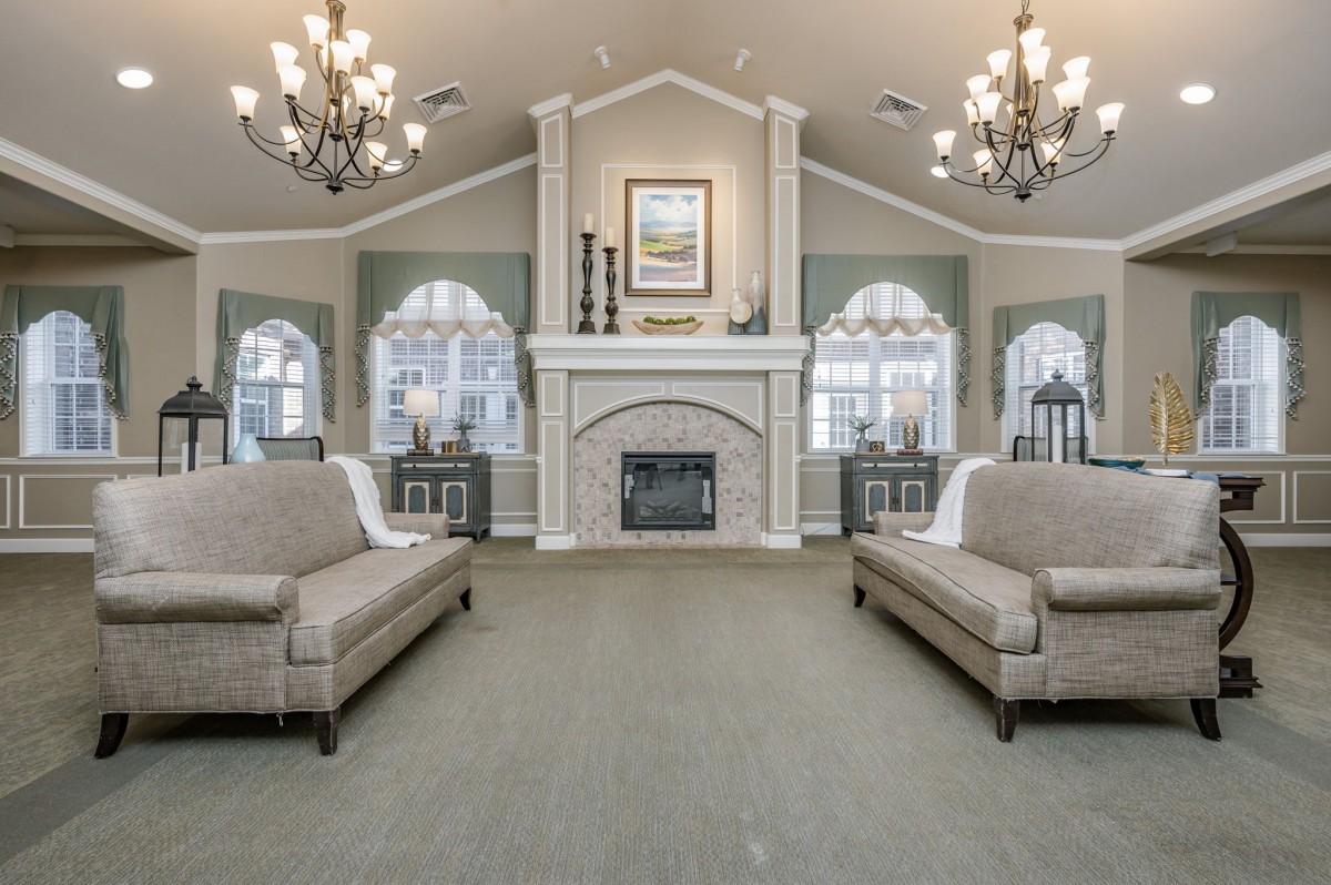 Elegant living room with a central fireplace and stylish chandeliers, featuring sofas and arched windows.