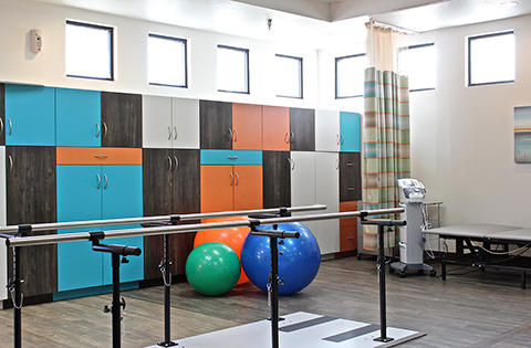 A well-equipped rehabilitation therapy room featuring colorful storage, exercise balls, and barre for physical therapy.