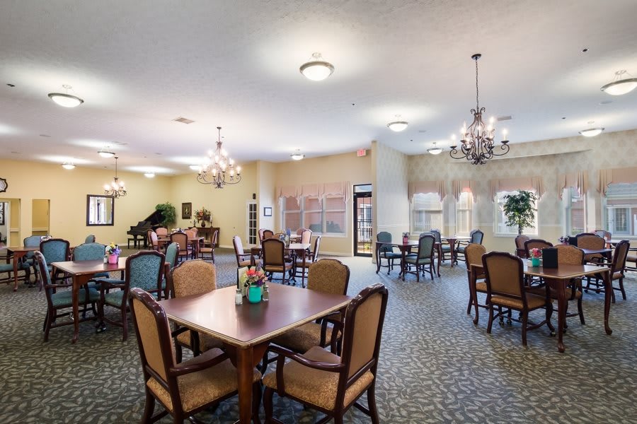 A spacious and well-lit dining room featuring multiple tables and chairs with elegant chandeliers.