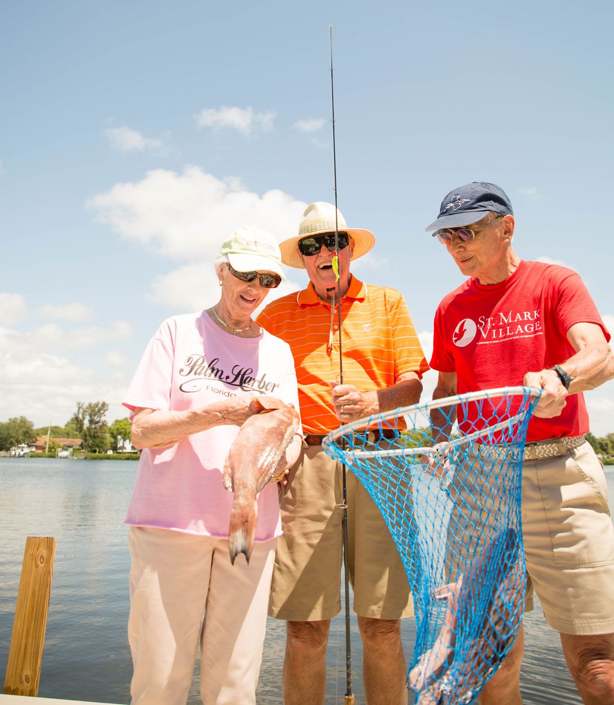 Three people standing by a lake holding a fishing net on a sunny day.