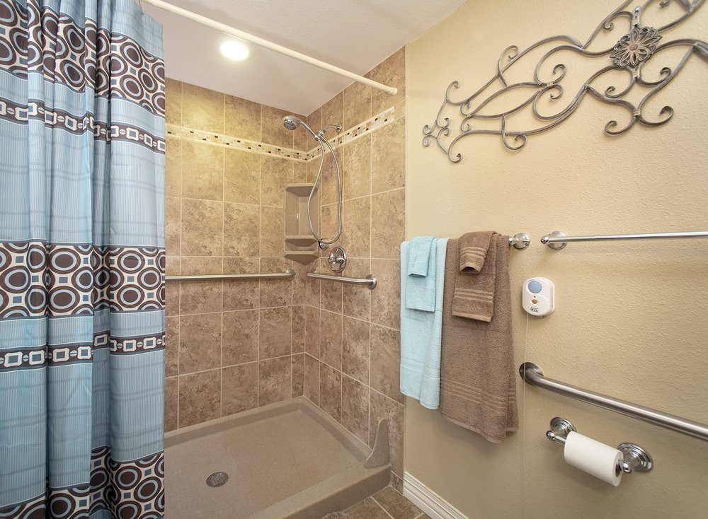 A well-designed bathroom featuring a tiled walk-in shower with grab bars and neatly hung towels.