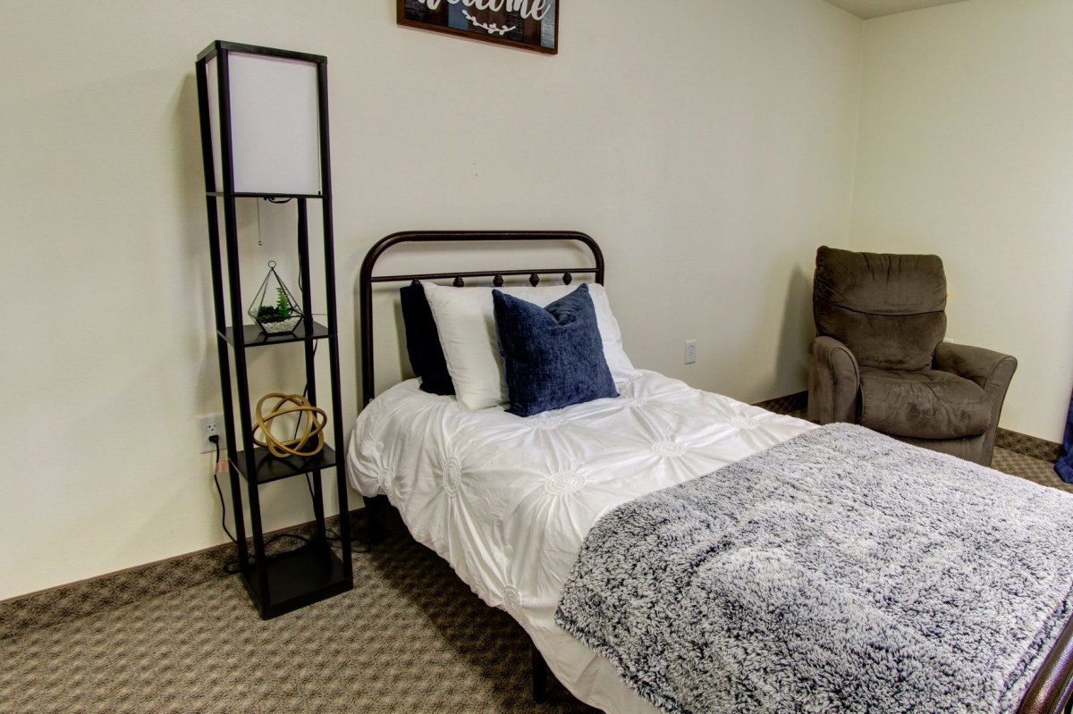 A cozy bedroom featuring a single bed with white bedding and a blue pillow, complemented by a black metal frame and a nearby floor lamp.
