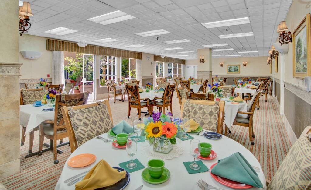 A beautifully set dining room with decorated tables and chairs, featuring colorful flowers and neatly arranged napkins.