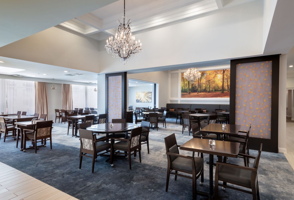 An elegant dining area featuring a chandelier, artwork, and neatly arranged tables and chairs.