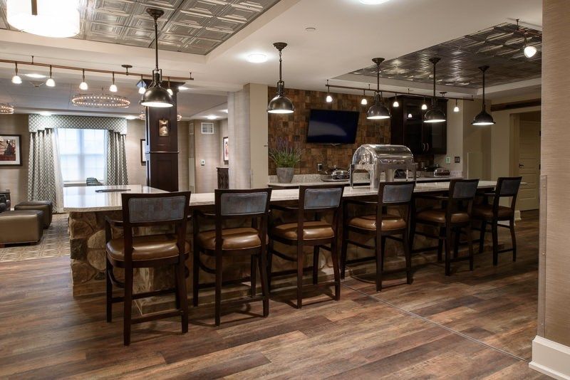 A modern bar interior with a long counter and high stools, complemented by warm lighting and wood flooring.