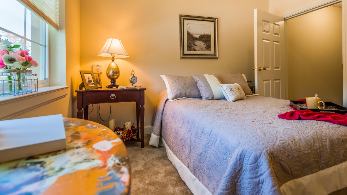 A cozy bedroom featuring a neatly made bed, a warm lamp on the nightstand, and tasteful decor.