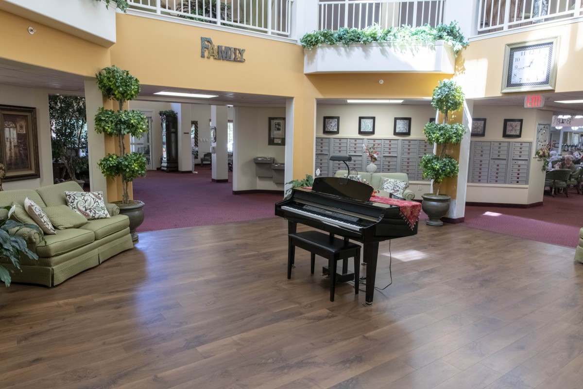 A spacious lobby area featuring a piano, surrounded by plants and comfortable seating.