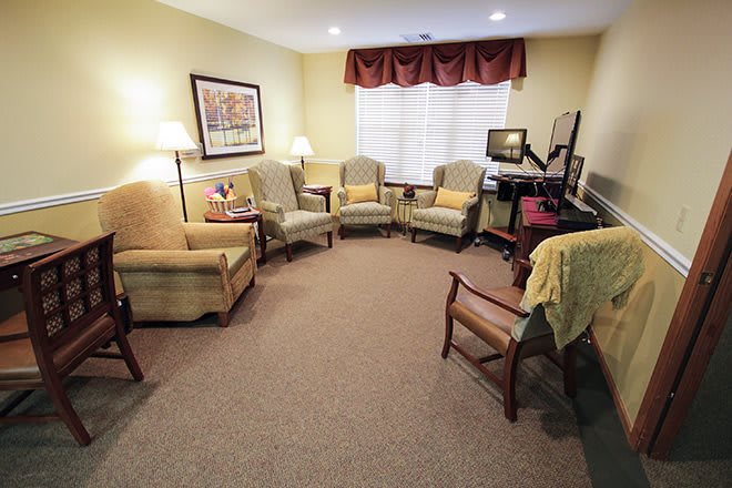 A cozy living room with several chairs arranged in a circular formation, featuring soft lighting and artwork on the walls.