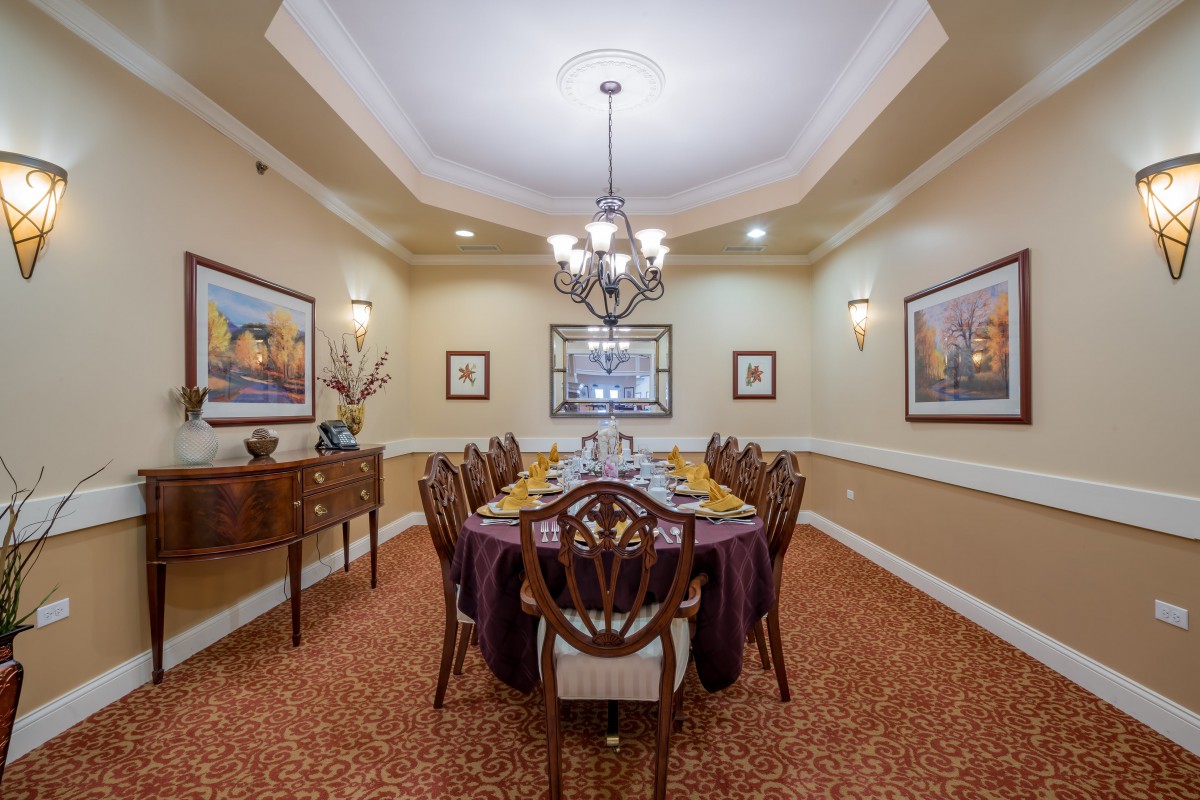 An elegant dining room with a long formal table, chandelier, and artwork on the walls.