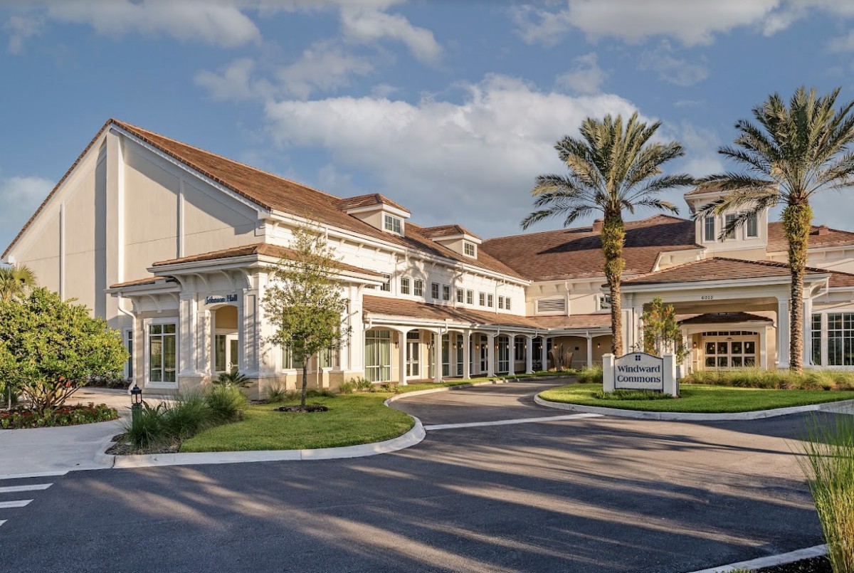 A sunny view of a residential building with palm trees and a driveway.