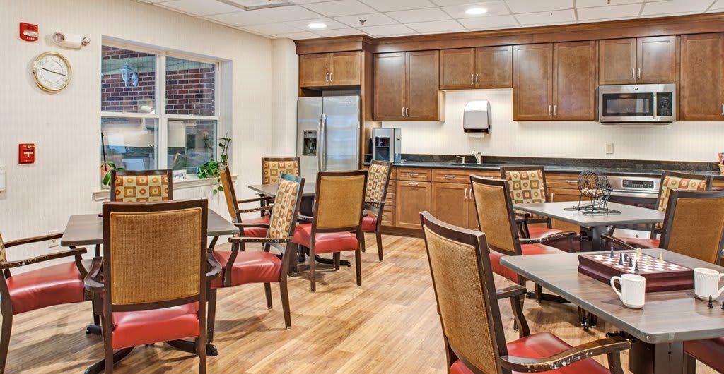 A modern dining area with wooden chairs and tables, featuring a kitchen setup with stainless steel appliances.