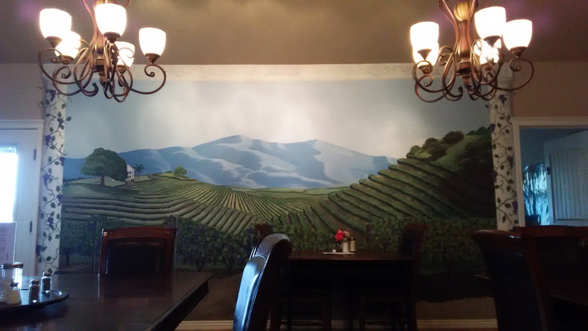 A cozy restaurant interior featuring a mural of rolling vineyards under chandeliers.