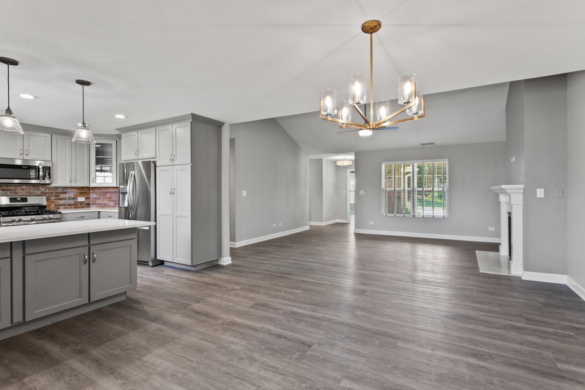 Modern open floor plan with a spacious kitchen and living area featuring hardwood floors and a stylish chandelier.