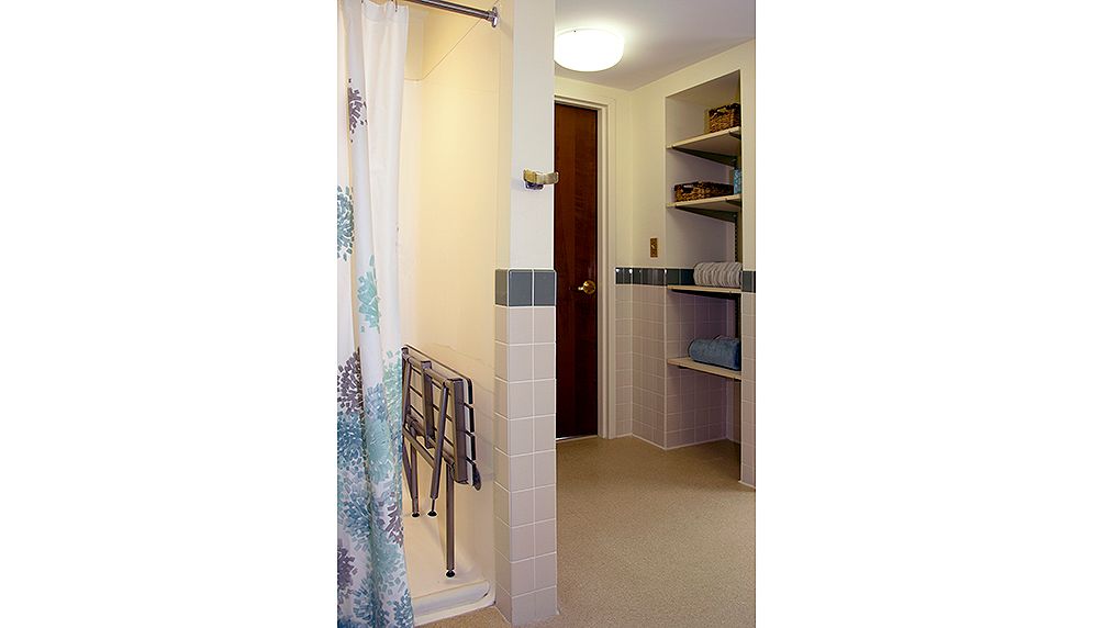A bathroom featuring an open shower, neatly organized towels on shelves, and a wooden door.