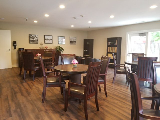 A cozy dining room with wooden tables and chairs, decorated with wall art and illuminated by ceiling lights.