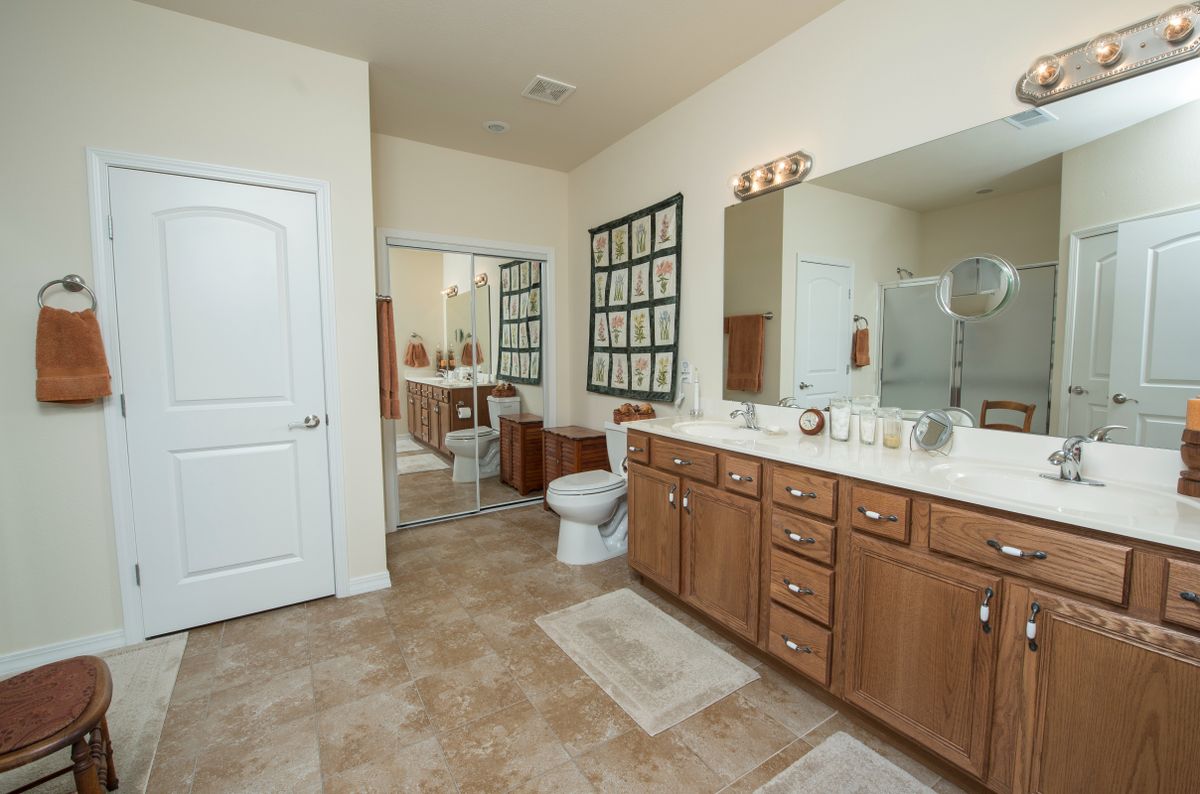 A spacious bathroom with wooden cabinets, a large mirror, and tiled flooring.