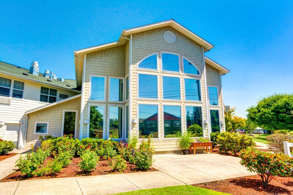 A modern house with large windows and well-maintained landscaping on a sunny day.