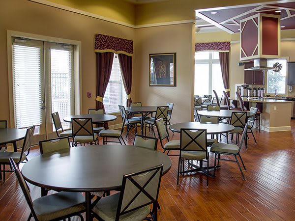 A cozy dining area with round tables and chairs, featuring wood flooring and large windows with curtains.