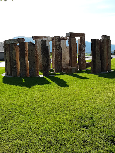 A view of a stone circle, reminiscent of ancient structures, surrounded by lush green grass under clear blue skies.