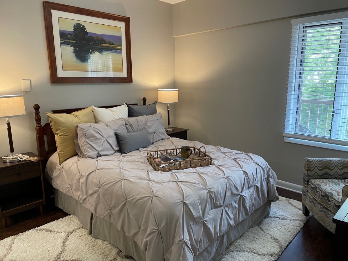 A cozy bedroom with stylish decor, featuring a neatly made bed, a bedside lamp, and framed artwork on the wall.